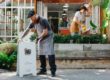 Homme barbu roux avec un béret et un tablier qui installe le panneau signalétique de son restaurant